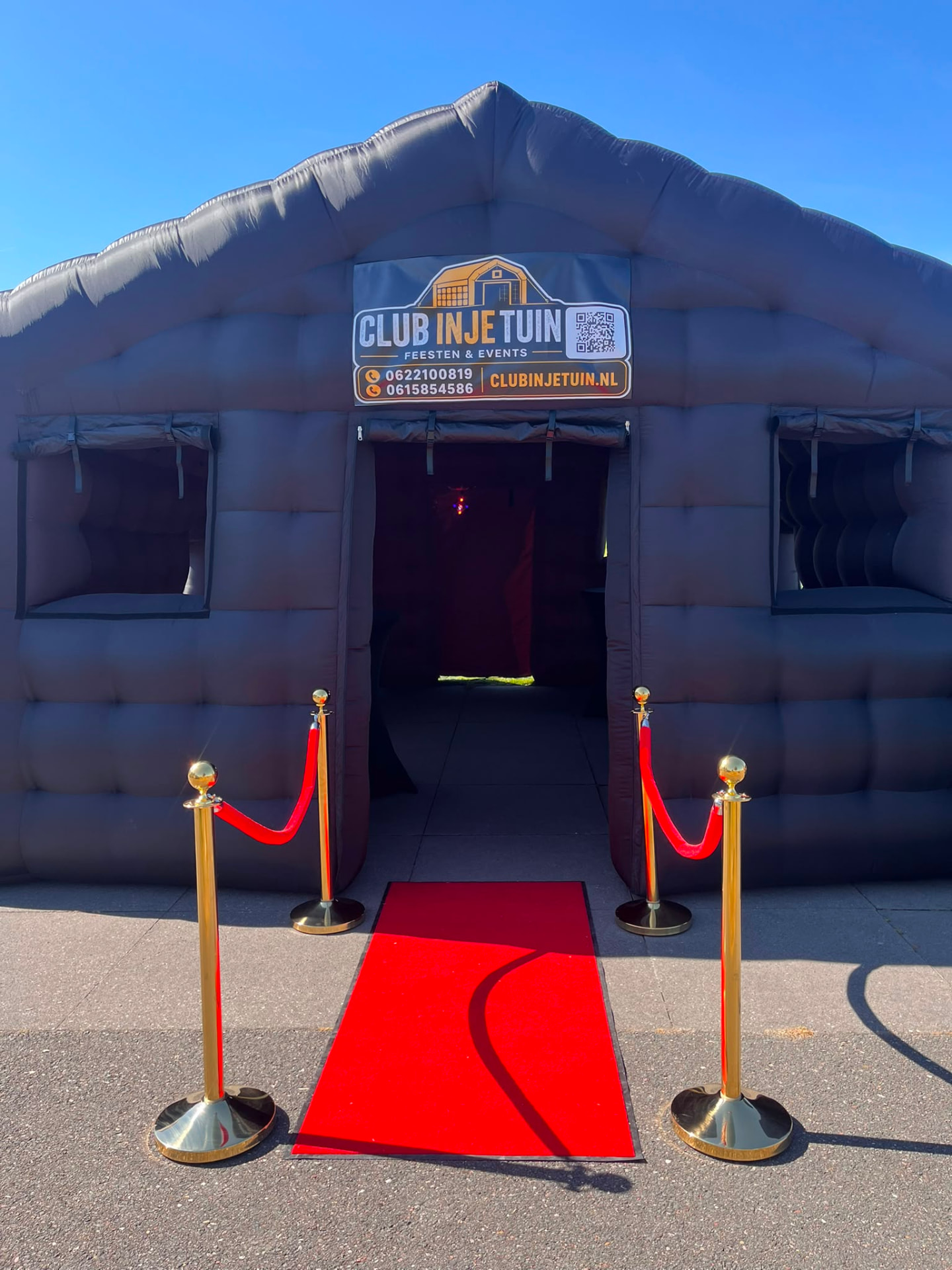 Ingang van de opblaasbare partytent met rode loper en logo Club in je Tuin