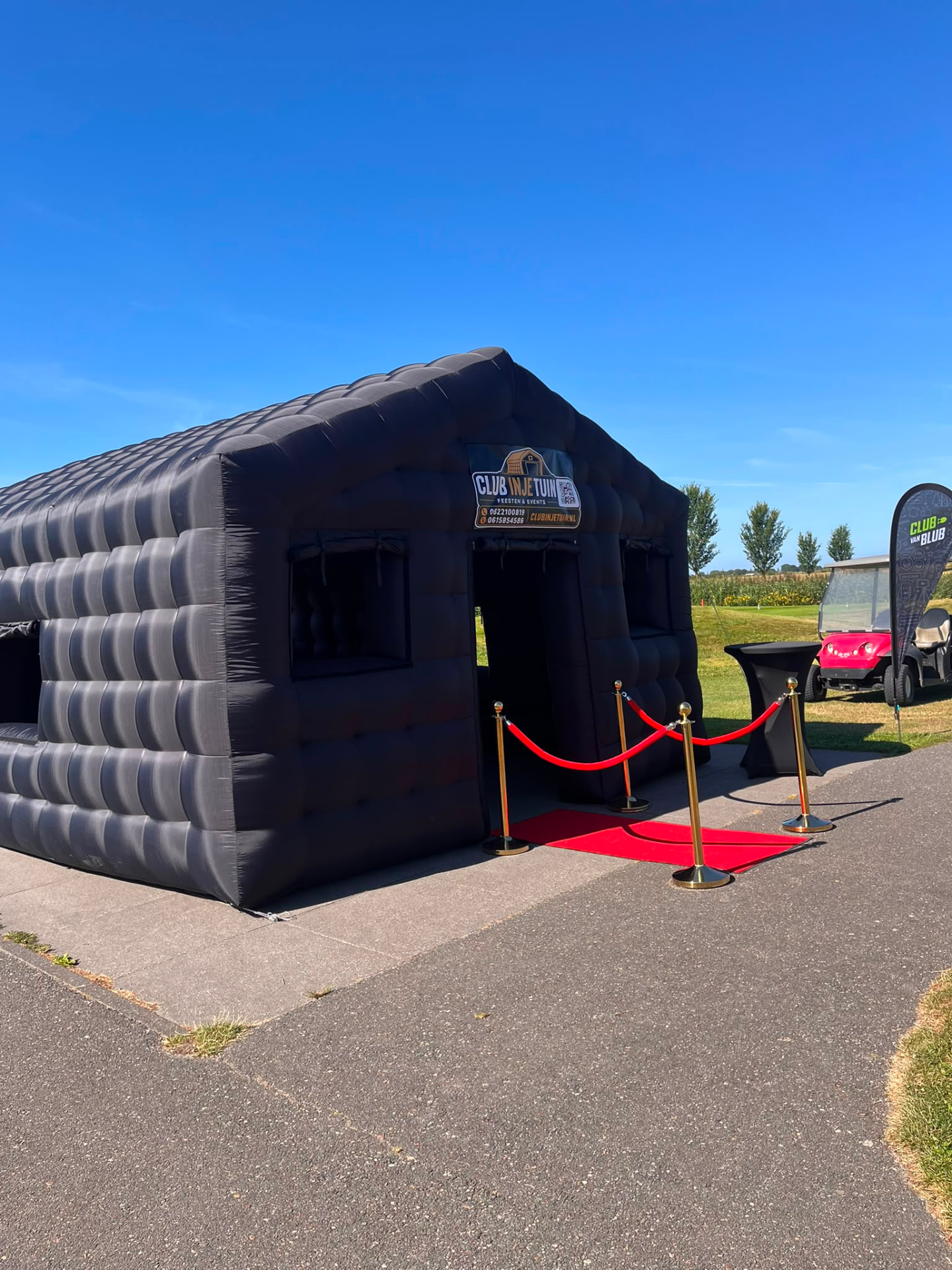 Opblaasbare partytent zwart op golfbaan met rode loper en gouden afzetpaaltjes