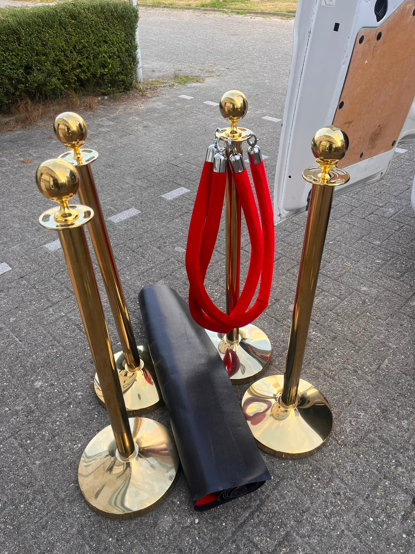 Vier gouden afzetpaaltjes met rood fluwelen koord en opgerolde rode loper