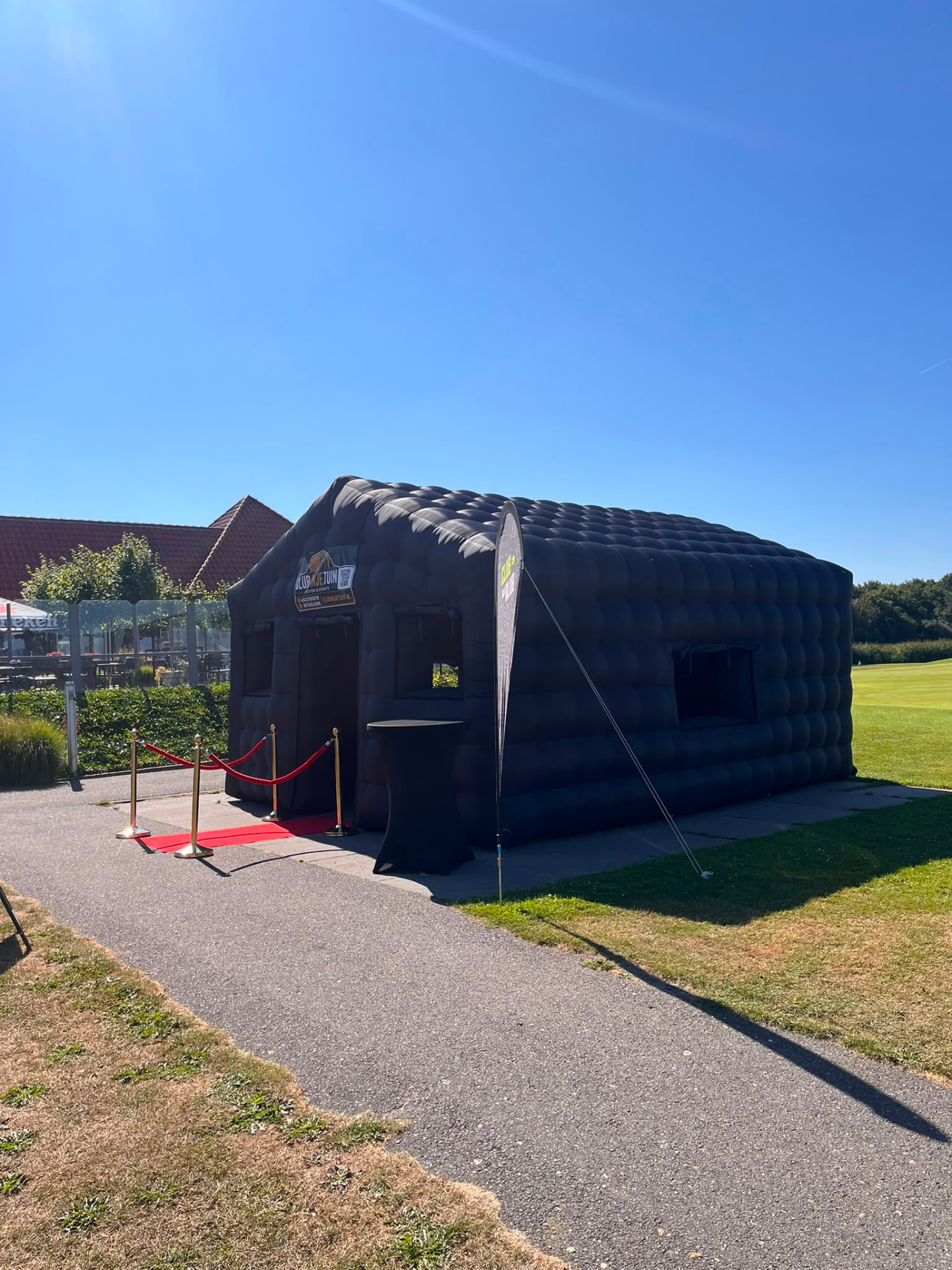 Zwarte opblaasbare partytent met rode loper en statafel bij golfbaan